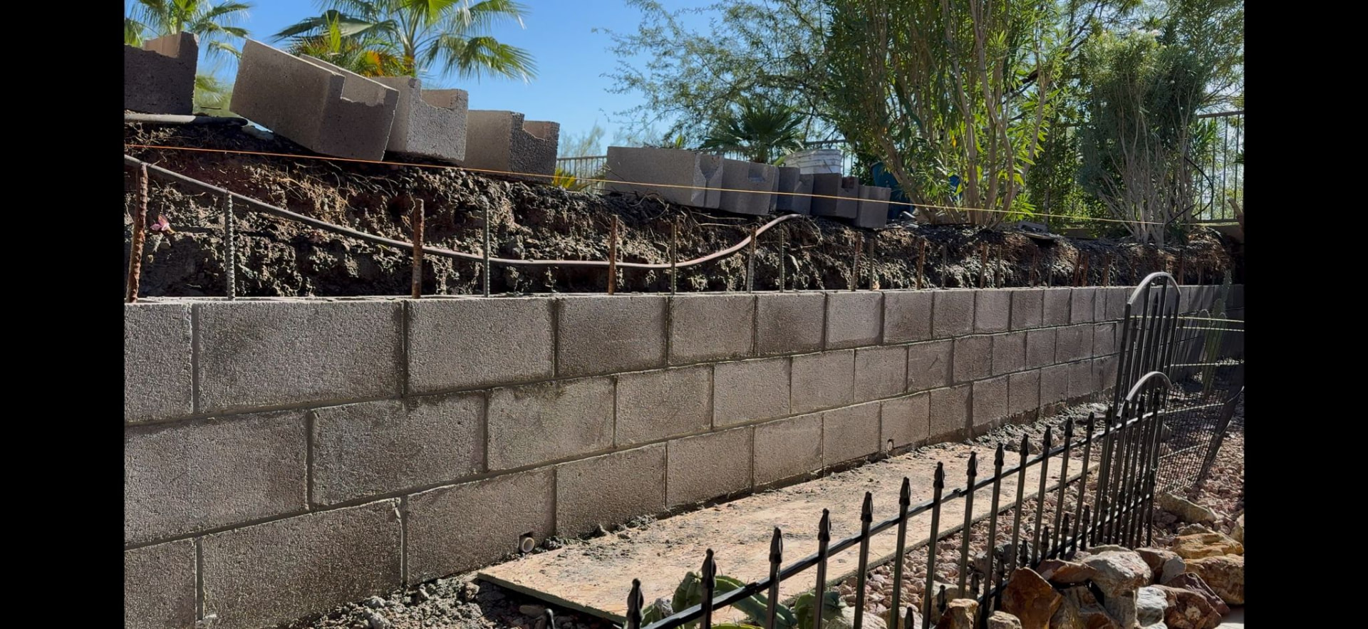 Block retaining wall under construction with rebar and footing along a sloped property line